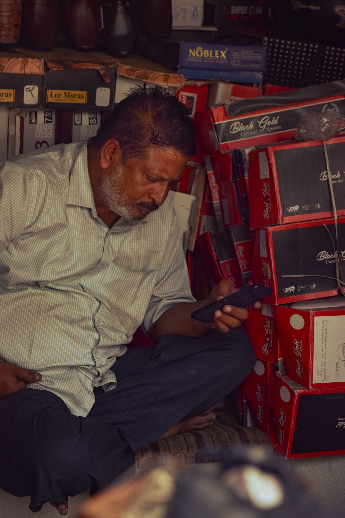 A small shop owner using a smartphone among stocked shelves